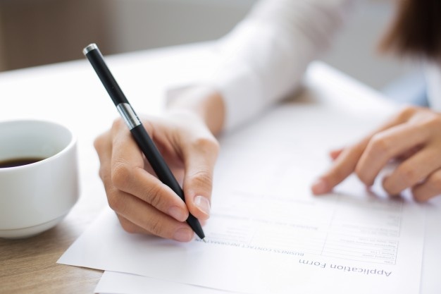 Image shows a person writing on a form.